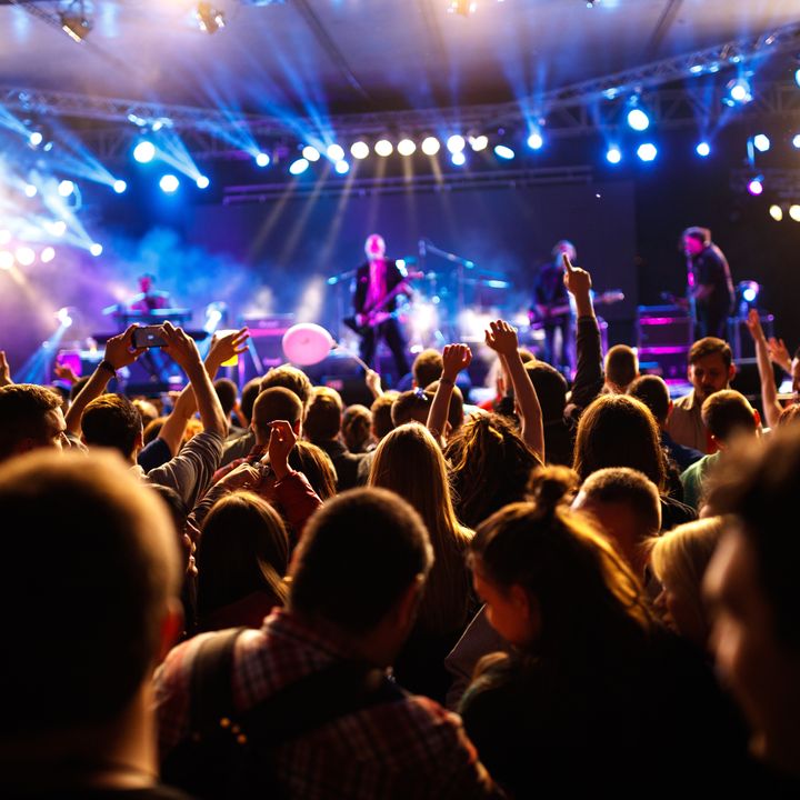 An eye-level view of a stage with a bunch of people with hands in the air at a concert.