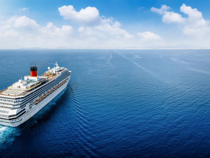 An aerial view over a cruise ship that is seen sailing along an empty blue sea.