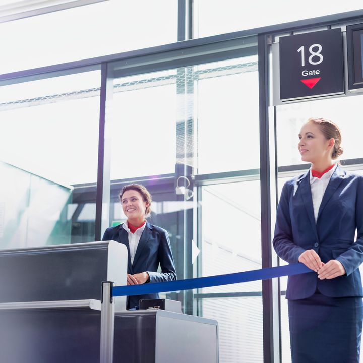 An airline gate agent stands at the gate door with tape partially closing it while another one stands at the desk.