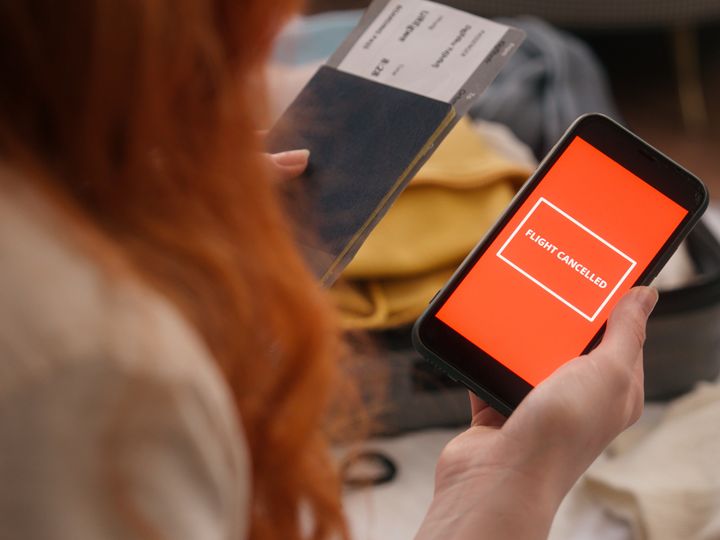 A woman whose face is not visible is seen holding a passport and a phone that says ‘flight canceled’ on the screen.