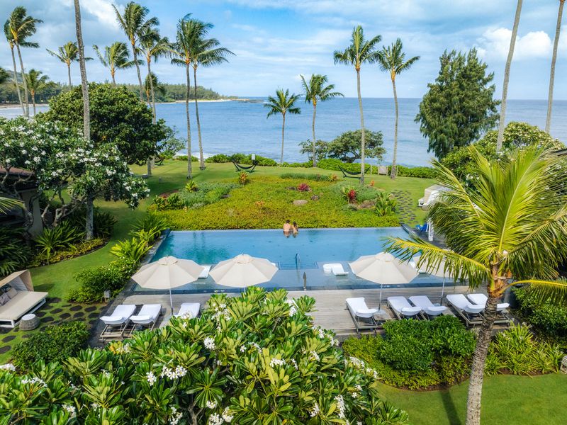An infinity edge pool with two people alone at the edge surrounded by lush tropical landscaping and ocean views.