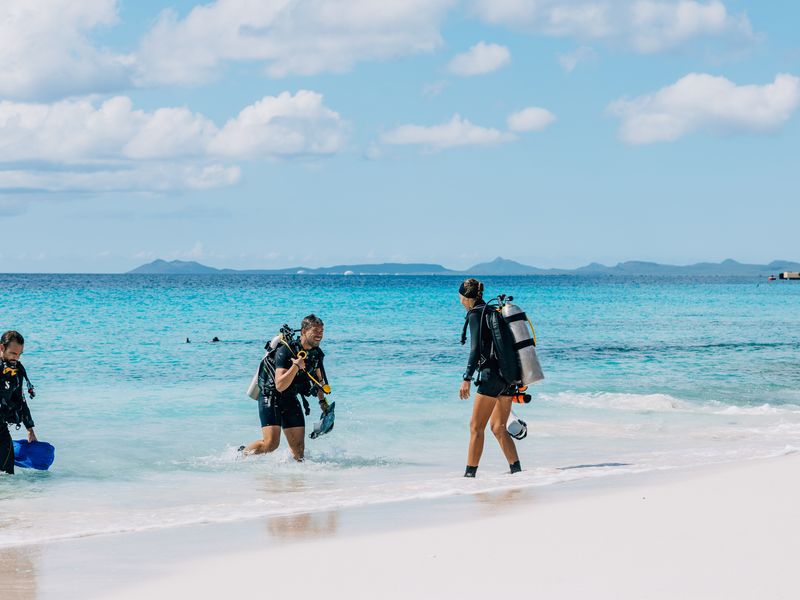Three scuba divers emerging from the blue waters on a tropical beach in Bonaire.